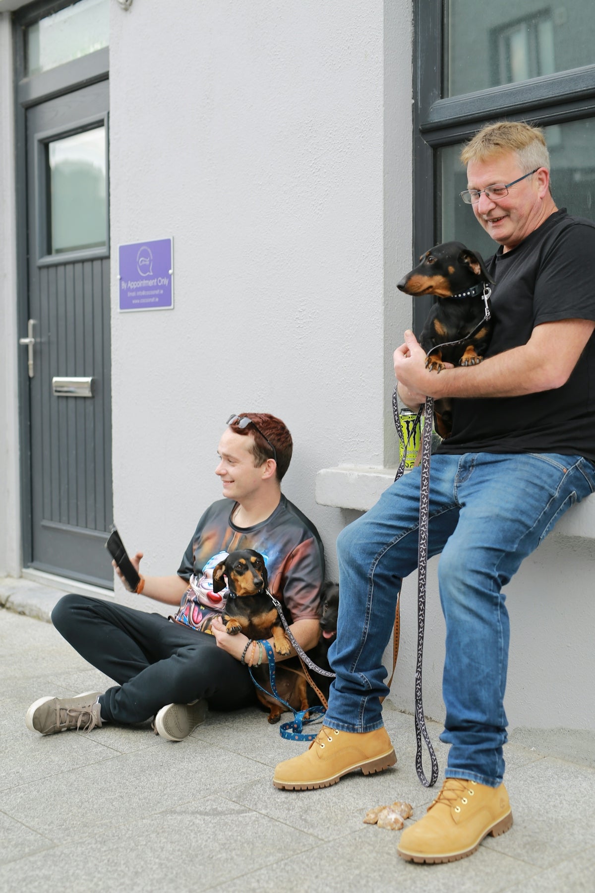 Two men holding dachshunds outside building